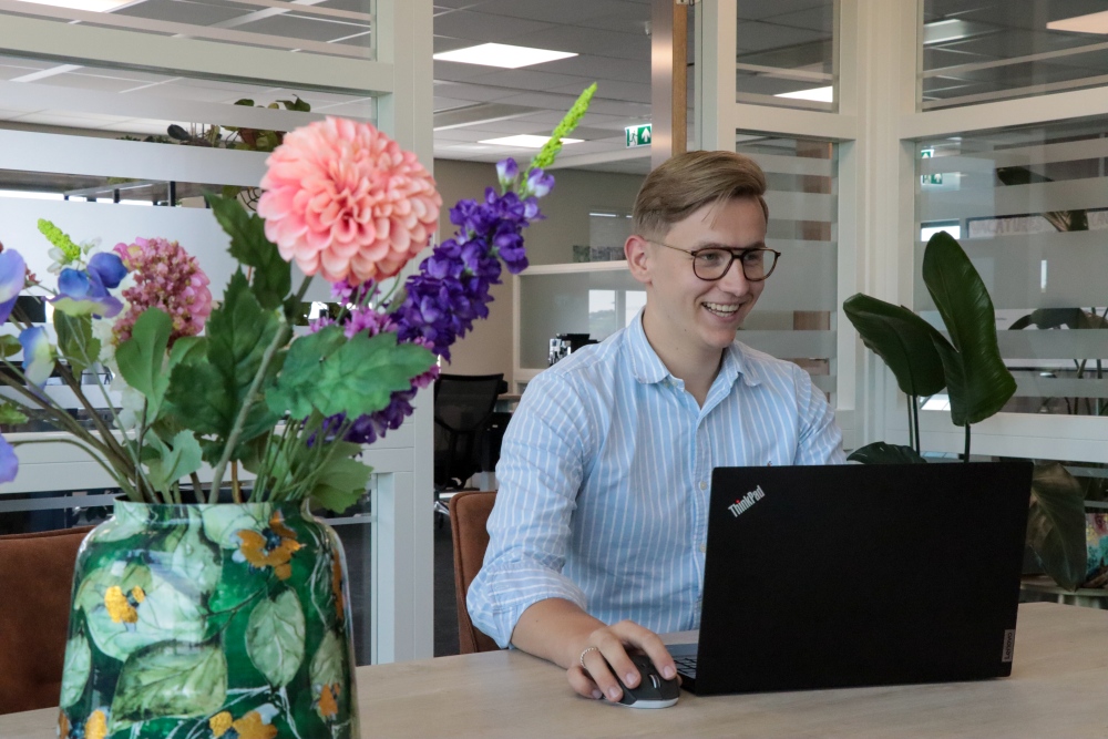 Aron van Intro Personeel achter zijn laptop en lacht in de camera